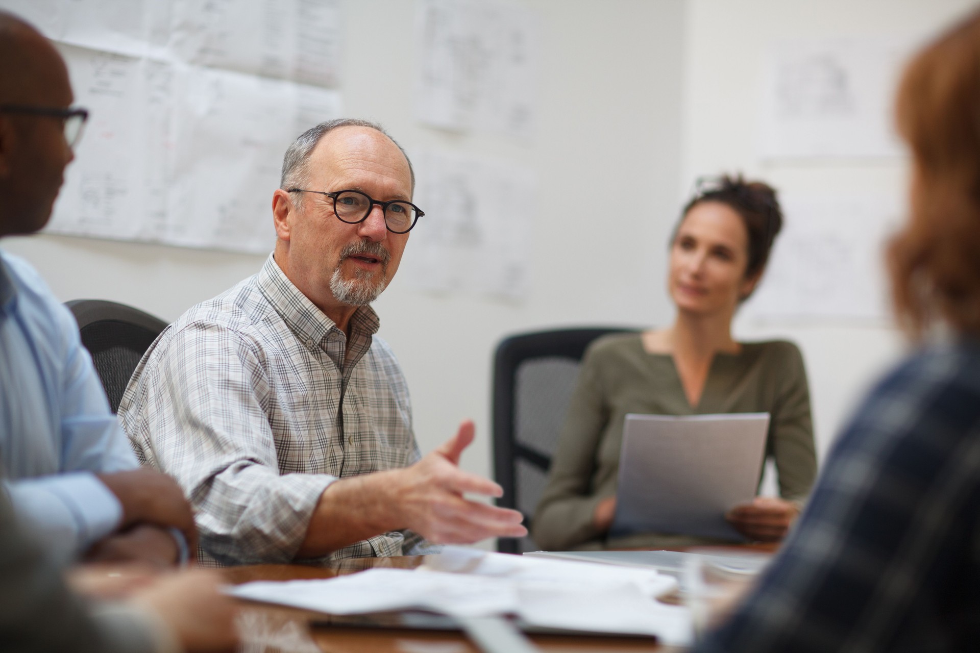 Senior man talks serious explaining in meeting with work colleagues while sitting at table in design office